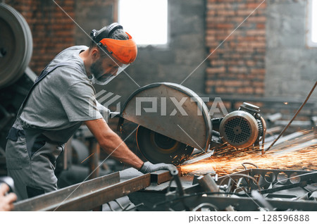 Side view, cutting the metal. Young factory worker in grey uniform Side view, cutting the metal. Young factory worker in grey uniform 128596888