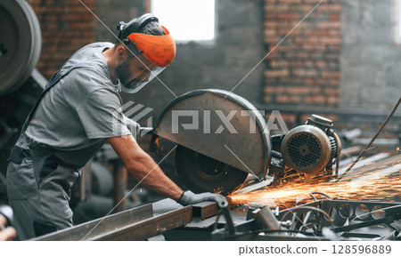Side view, cutting the metal. Young factory worker in grey uniform 128596889