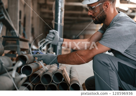 Sitting and working. Young man at the factory in grey uniform Sitting and working. Young man at the factory in grey uniform 128596936