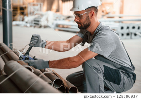 Sitting and working. Young man at the factory in grey uniform Sitting and working. Young man at the factory in grey uniform 128596937