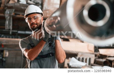 Moving big metal pipe. Young factory worker in grey uniform 128596940