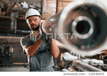 Moving big metal pipe. Young factory worker in grey uniform 128596941