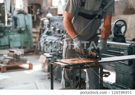 Polishing the surface with angle grinder. Close up view of man that is working at the factory 128596951