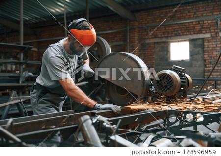 Process of cutting the metal. Young factory worker in grey uniform 128596959