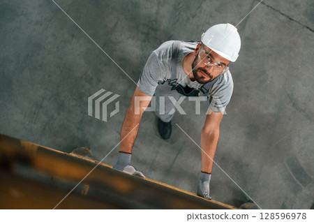 Going up on the ladder, top view. Young factory worker in grey uniform 128596978