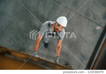 Going up on the ladder, top view. Young factory worker in grey uniform 128596979
