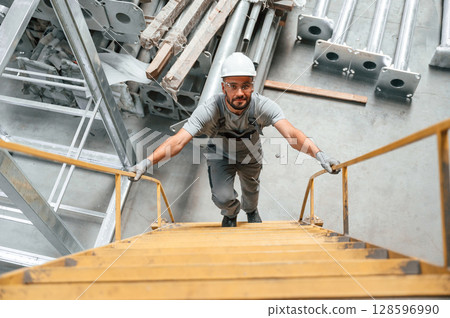 Climbing up on the ladder. Young factory worker in grey uniform Climbing up on the ladder. Young factory worker in grey uniform 128596990
