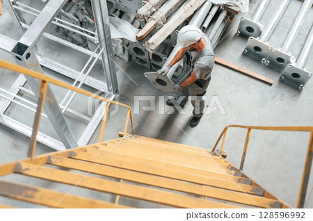 Climbing up on the ladder. Young factory worker in grey uniform Climbing up on the ladder. Young factory worker in grey uniform 128596992