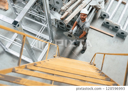 Climbing up on the ladder. Young factory worker in grey uniform Climbing up on the ladder. Young factory worker in grey uniform 128596993