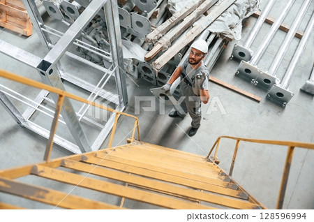 Climbing up on the ladder. Young factory worker in grey uniform 128596994