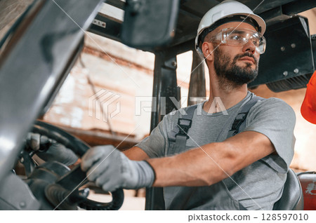 Professional forklift driver. Young factory worker in grey uniform 128597010