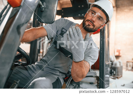 Hand gestures. In the forklift. Young factory worker in grey uniform 128597012