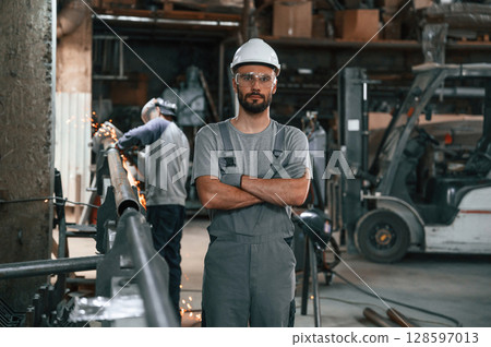 Another man is behind. Young factory worker in grey uniform 128597013