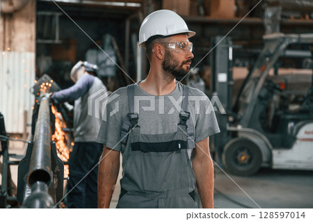 Another man is behind. Young factory worker in grey uniform Another man is behind. Young factory worker in grey uniform 128597014
