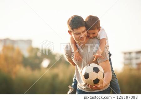 Holding professional soccer ball. Father and little son are playing and having fun outdoors Holding professional soccer ball. Father and little son are playing and having fun outdoors 128597098