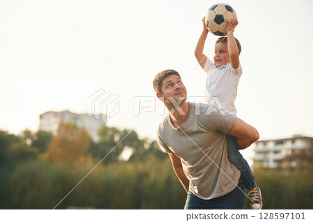 Holding professional soccer ball. Father and little son are playing and having fun outdoors 128597101