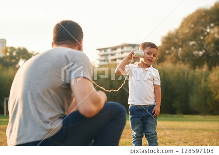 Talking by using string can phone. Father and little son are playing and having fun outdoors Talking by using string can phone. Father and little son are playing and having fun outdoors 128597103