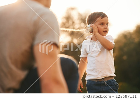 Fun, holding and using string can phone. Father and little son are playing outdoors Fun, holding and using string can phone. Father and little son are playing outdoors 128597111