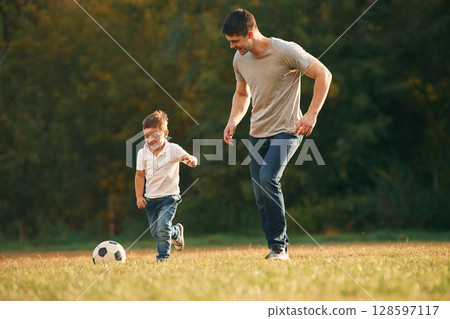 Smiling, running with soccer ball. Father and little son are playing and having fun outdoors Smiling, running with soccer ball. Father and little son are playing and having fun outdoors 128597117