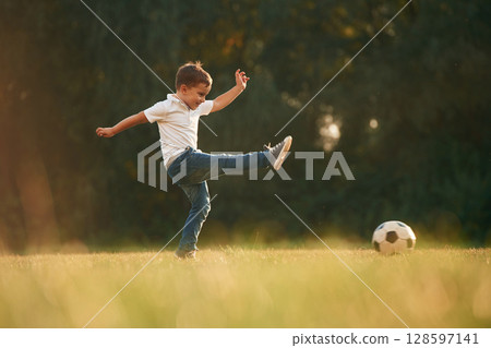 Side view, playing soccer. Little boy is playing outdoors at daytime Side view, playing soccer. Little boy is playing outdoors at daytime 128597141