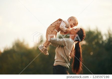 Holding kid in hands. Mother is with her little baby son are outdoors together Holding kid in hands. Mother is with her little baby son are outdoors together 128597190