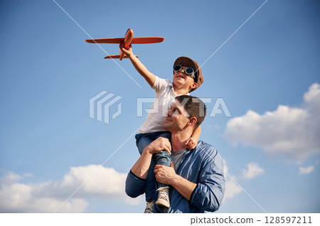 Playing with toy plane, sitting on the shoulders. Father and little son are having fun outdoors 128597211