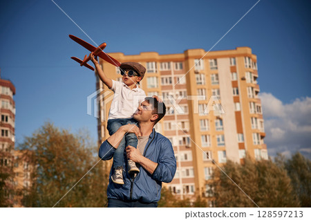 Playing with toy plane, sitting on the shoulders. Father and little son are having fun outdoors 128597213