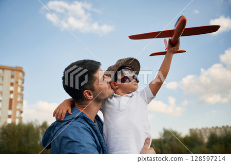 Playing with toy plane, sitting on the shoulders. Father and little son are having fun outdoors Playing with toy plane, sitting on the shoulders. Father and little son are having fun outdoors 128597214
