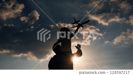 Against dramatic sky, with toy plane, sitting on shoulders. Father and little son are playing and having fun outdoors 128597217