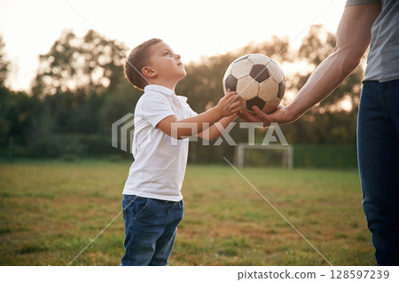 Boy is taking soccer ball. Father and little son are playing and having fun outdoors Boy is taking soccer ball. Father and little son are playing and having fun outdoors 128597239