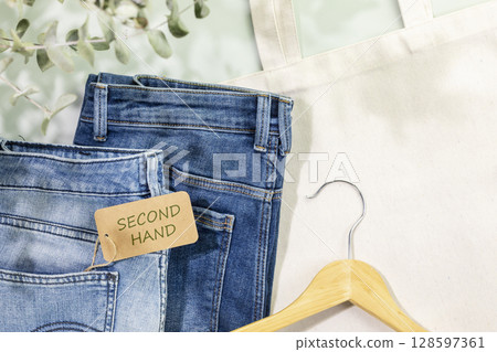 Sustainable still life with djinns with label Second Hand, textile bag and hanger. Second hand clothing shop. Circular fashion, eco friendly sustainable shopping, thrifty shop concept. Flat lay Sustainable still life with djinns with label Second Hand, textile bag and hanger. Second hand clothing shop. Circular fashion, eco friendly sustainable shopping, thrifty shop concept. Flat lay 128597361