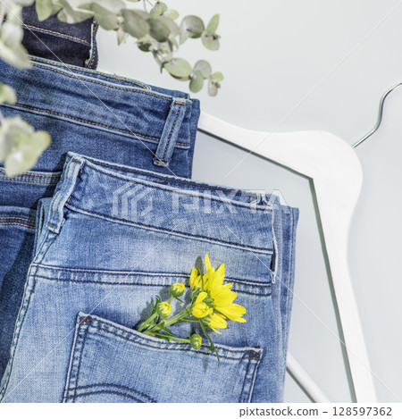 Romantic spring shopping banner with different kind of jeans with flower and white hanger on blue background. Denim clothing store. Spring sale. Casual wear. Flat lay 128597362
