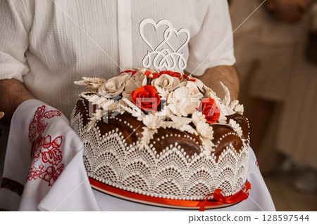 Traditional Ukrainian Wedding Cake with Heart Topper Held by Hands, Lace Decoration, Red Roses, Embroidery, Cultural Ceremony Details 128597544
