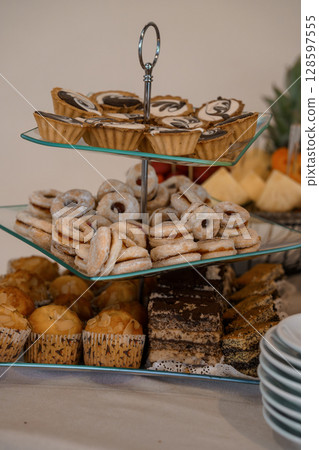 A Lavish Dessert Display on a Glass Tier Stand Featuring Mini Pastries, Cookies, and Brownies at an Elegant Event. A Lavish Dessert Display on a Glass Tier Stand Featuring Mini Pastries, Cookies, and Brownies at an Elegant Event. 128597555