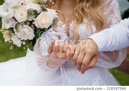 Wedding Rings Exchange: Close-up of Bride and Groom Hands, White Bouquet, Golden Bands, Love, Marriage, Traditional Ceremony, Soft Focus, Natural Light 128597566
