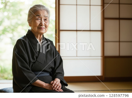 Portrait of a graceful elderly japanese woman in a black kimono sitting in a traditional room 128597796