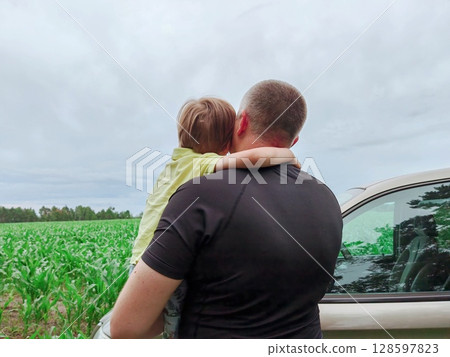 Father and son on the field on the background nature. Happy family and parental love concept. Dad holds his son in his arms. Family car trip. Father and son on the field on the background nature. Happy family and parental love concept. Dad holds his son in his arms. Family car trip. 128597823
