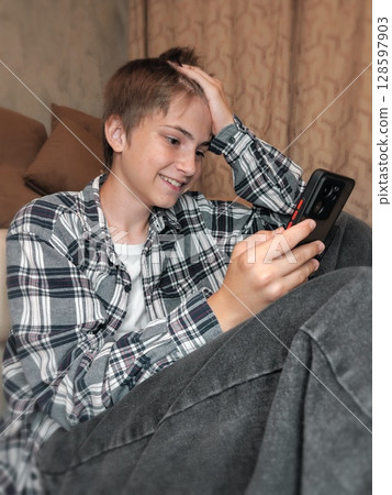 young guy using a mobile phone. Shocked teenager using mobile phone at home 128597903