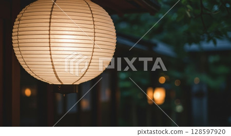 Japanese paper lantern glowing softly at dusk in a traditional garden setting with warm bokeh 128597920
