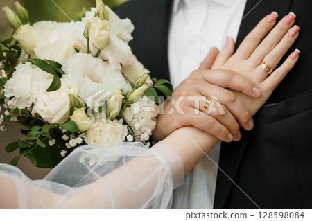 Wedding Hands with Gold Rings Bouquet: Romantic Couple Celebrating Marriage, White Flowers, Black Suit, First Love, Luxury Detail and Soft Focus 128598084