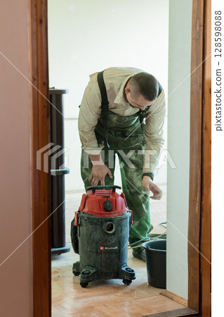 Man Cleaning Dust with Vacuum in Home Renovation, Hardwood Floor, Toolbox, Red Vacuum Cleaner, Indoor Shot, Dusty Workspace 128598088