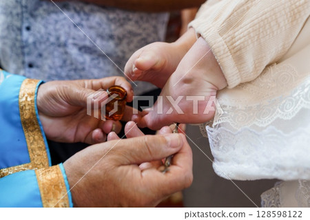 Anointing of Baby's Foot During Christian Baptism Ceremony, Hands with Oil, White Robe, Religious Ritual, Gold Accents, Soft Lighting 128598122