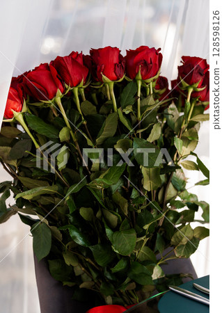 Vibrant Red Roses Bouquet in Brown Vase. Close-Up of Long-Stemmed Flowers. Romantic Gesture. Lush Floral Arrangement. Dark Green Foliage. Vibrant Red Roses Bouquet in Brown Vase. Close-Up of Long-Stemmed Flowers. Romantic Gesture. Lush Floral Arrangement. Dark Green Foliage. 128598126