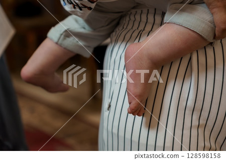 Intimate Father-Son Moment: Barefoot Baby Held in Dad's Lap, Striped Pajamas, Soft Lighting, Warm Indoor Scene, Family Love, Tender Care, Cozy Mood. 128598158