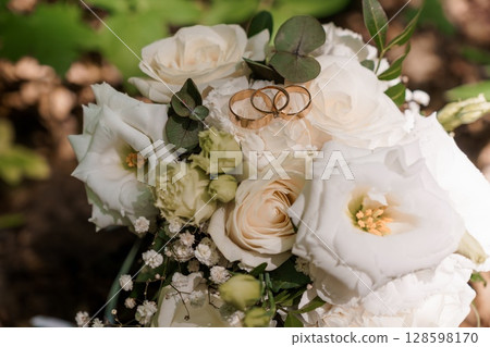 Elegant Wedding Rings on a White Rose Bouquet, Romantic Scene with Greenery and Natural Light, Luxury Marriage Symbolism, Floral Arrangement. Elegant Wedding Rings on a White Rose Bouquet, Romantic Scene with Greenery and Natural Light, Luxury Marriage Symbolism, Floral Arrangement. 128598170