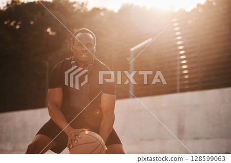 Sunlight outdoors. Young black man is with basketball ball Sunlight outdoors. Young black man is with basketball ball 128599063