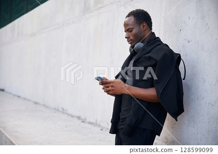 With headphones. Handsome black man is posing outdoors at daytime With headphones. Handsome black man is posing outdoors at daytime 128599099