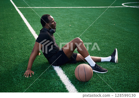 Sitting and relaxing. Young black man is with basketball ball outdoors Sitting and relaxing. Young black man is with basketball ball outdoors 128599130