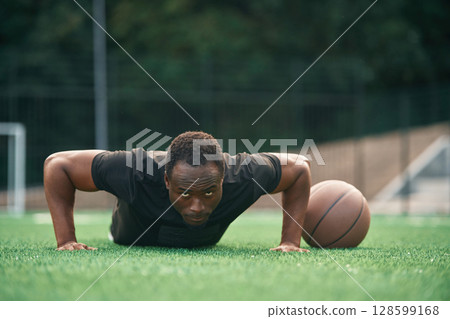 Doing push ups. Young black man is with basketball ball outdoors Doing push ups. Young black man is with basketball ball outdoors 128599168