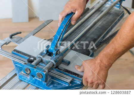 Worker skillfully operates tile cutter, shaping ceramic tiles during home renovation 128603887